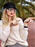 Woman wearing a black cap and glasses, pointing with both hands outdoors.