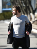 Man walking outdoors wearing a light gray t-shirt and dark jacket.