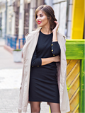 Woman in a black dress and beige trench coat standing against a colorful background