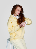 Woman in a yellow hoodie and pants sitting on a stool, looking at her wrist.